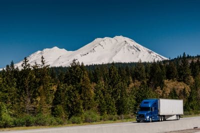 Semi truck driving on a highway with a snow-capped mountain in the background